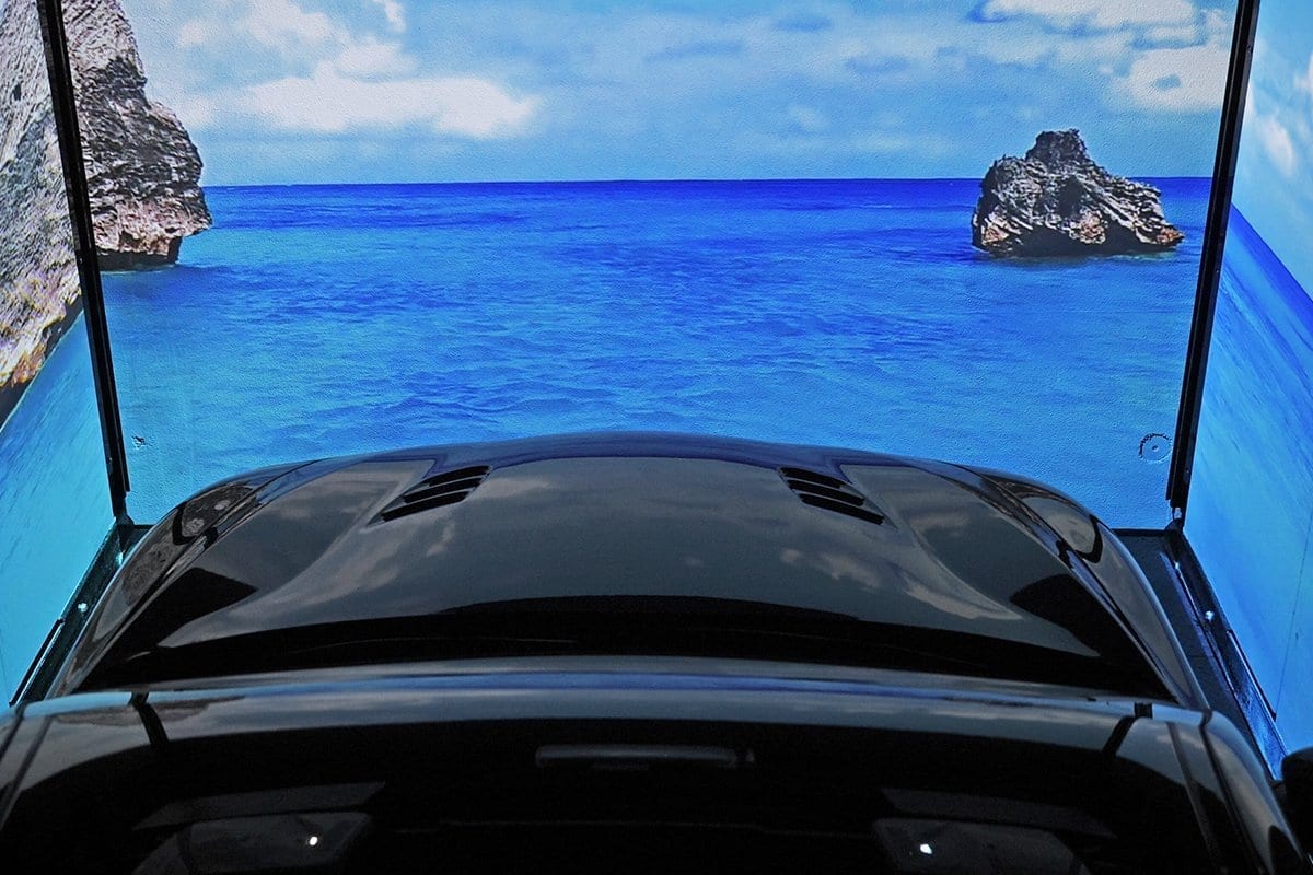 Black car seen from inside with open panoramic roof, view of blue sea with rocks and blue sky
