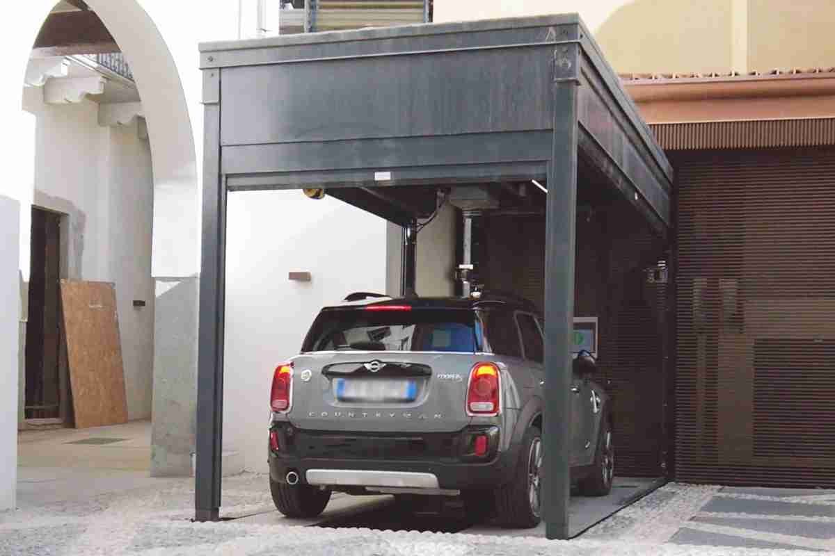 Grey car parked under grey metal structure with roof, inner courtyard with residential buildings